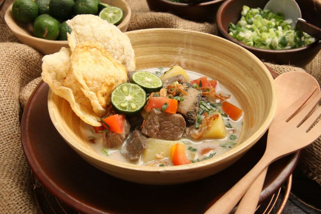 Semangkuk soto daging kuah bening dengan irisan daging sapi empuk, tauge, daun bawang, seledri, bawang goreng, dan jeruk nipis siap disajikan hangat.